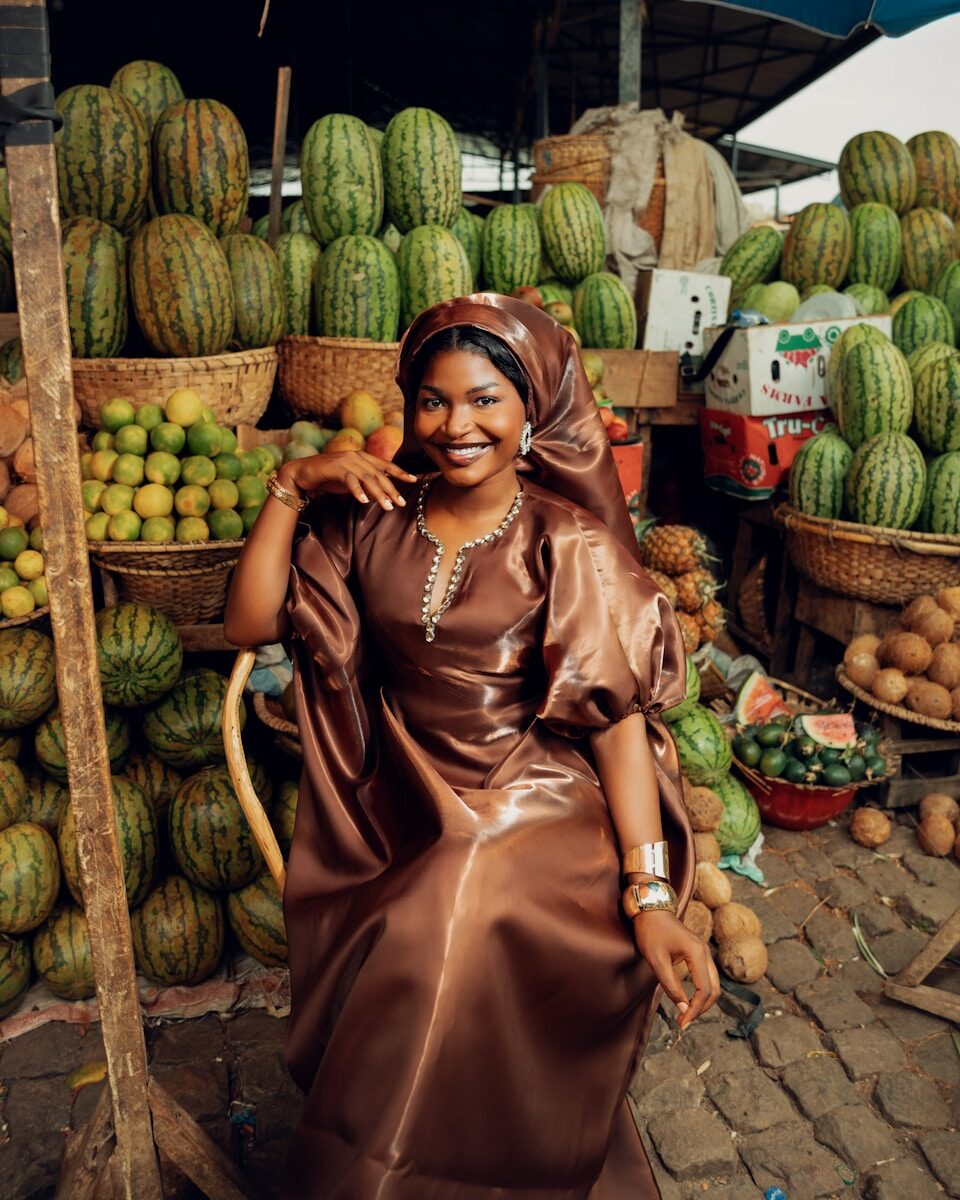 A smiling woman sits in a fruit market.